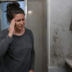 욕실 벽의 곰팡이를 바라보며 관자놀이를 짚고 두통을 느끼는 서양인 여성